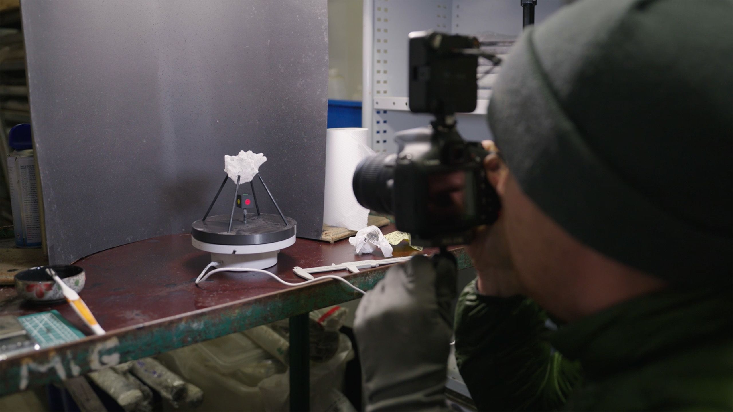 A person is crouched down behind a camera, shooting pictures of a white hailstone mounted on a stand.