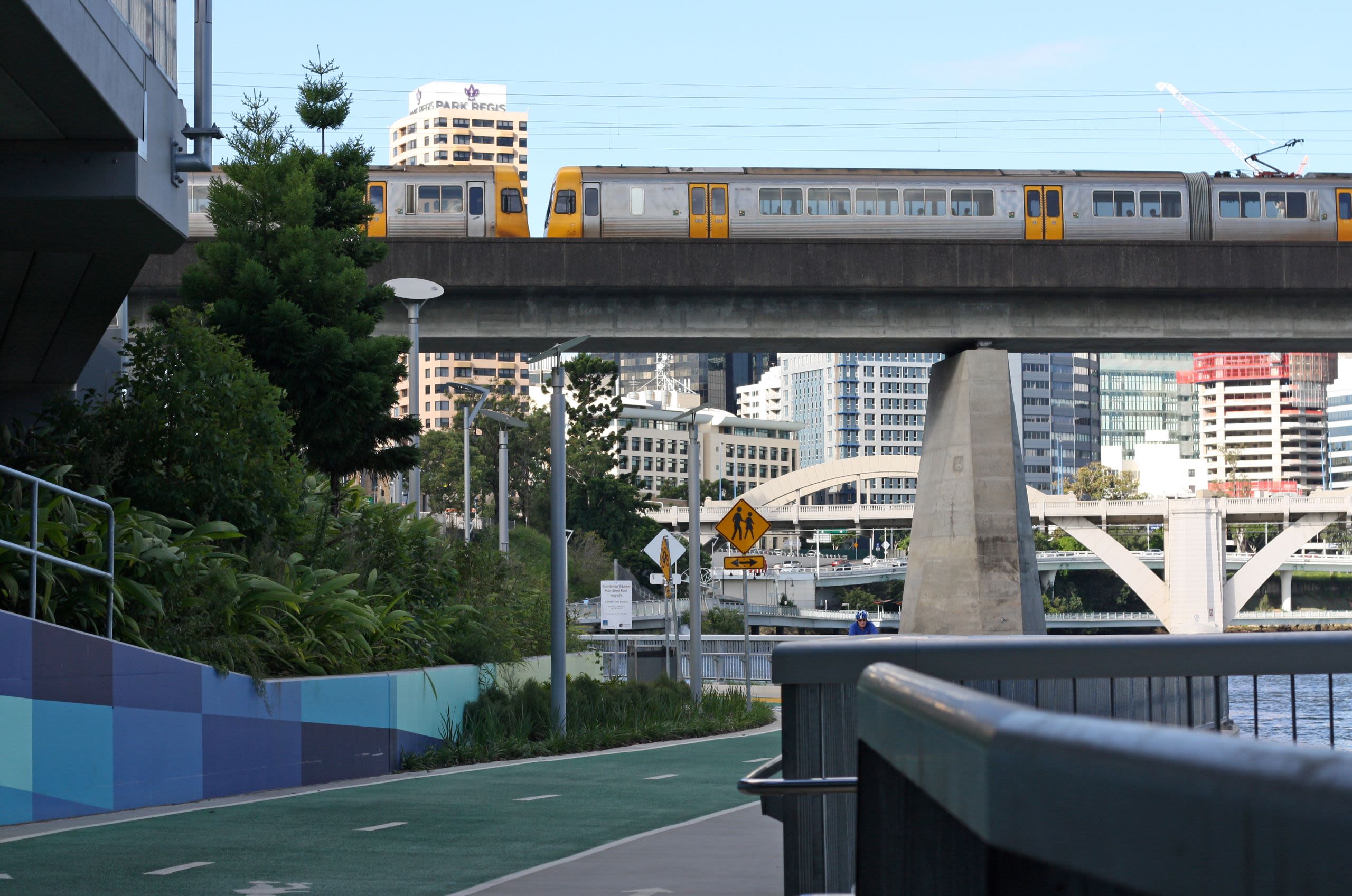 A train crossing a bridge above a cycle path next to a river