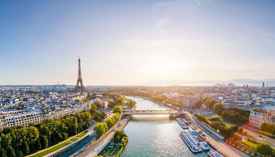 A view of Paris from above, featuring the Eiffel Tower, a bridge crossing the River Seine, and many old buildings