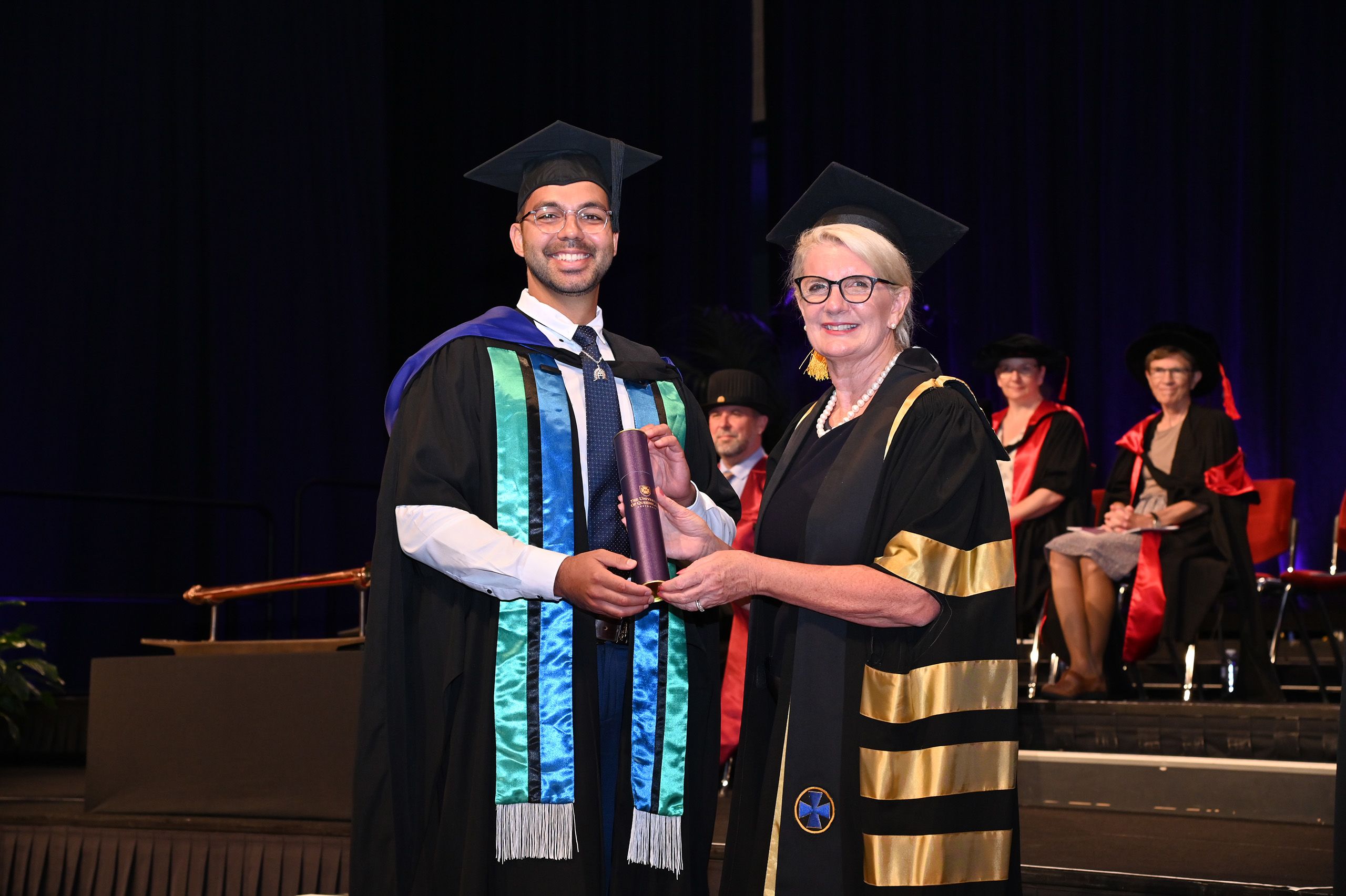 A man in a graduation cap and grown holding a cylinder