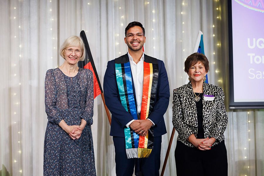 Two women and a young man posing in front of the camera, the young man wearing a sash representing the Aborignal and Torres Strait Islander flags
