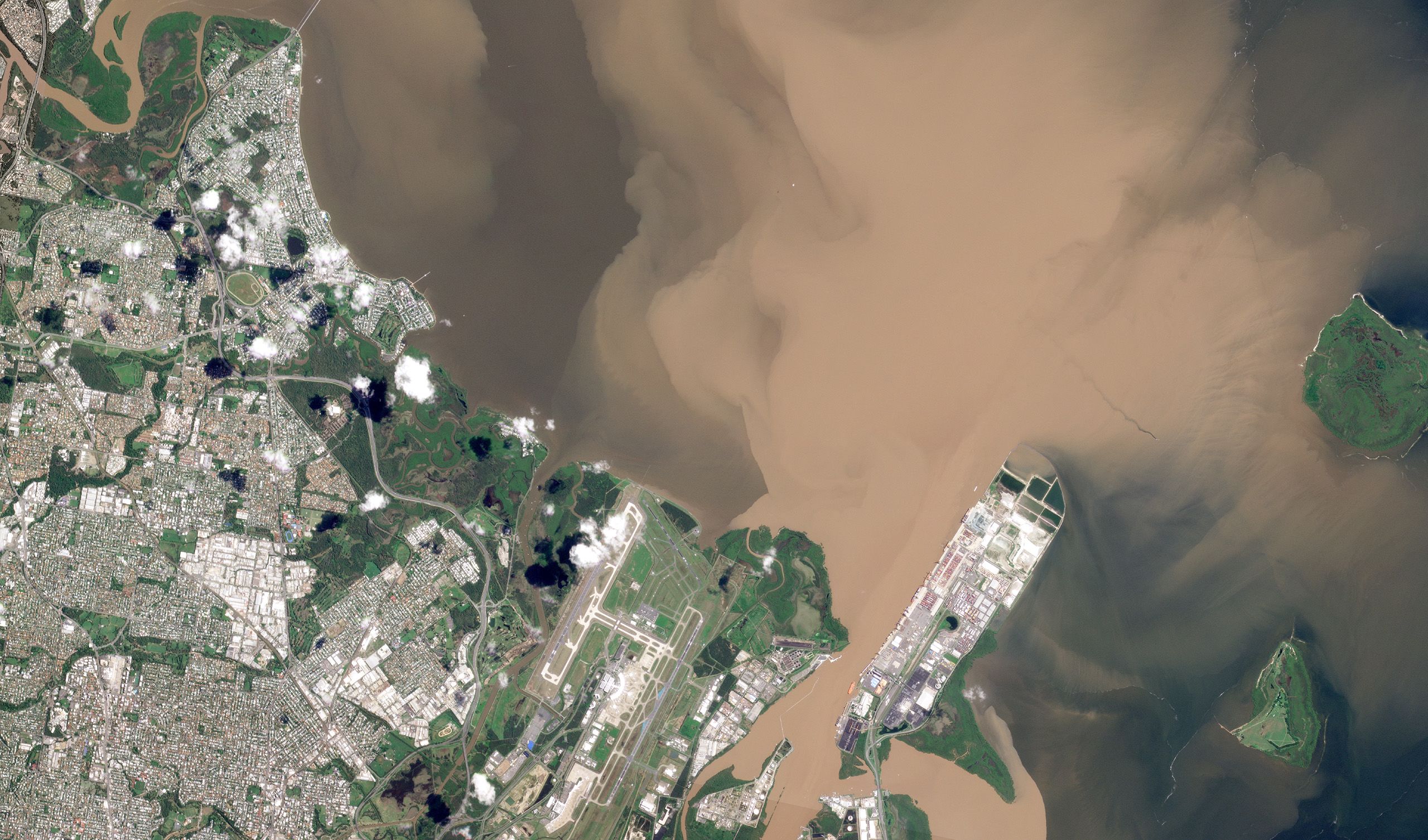 aerial view of city and airport next to a river with brown water visible