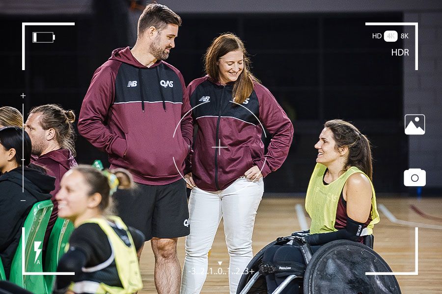 Two QAS coaching staff talk to a wheelchair rugby player during a training session.