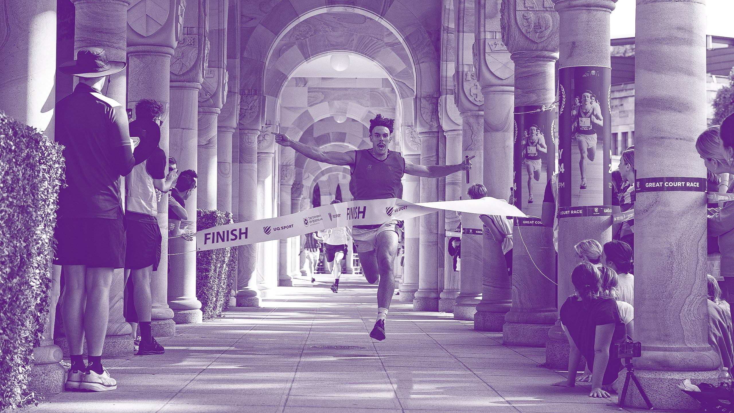 A male runner crosses the finish line in the Great Court Race with his arm outstretched.