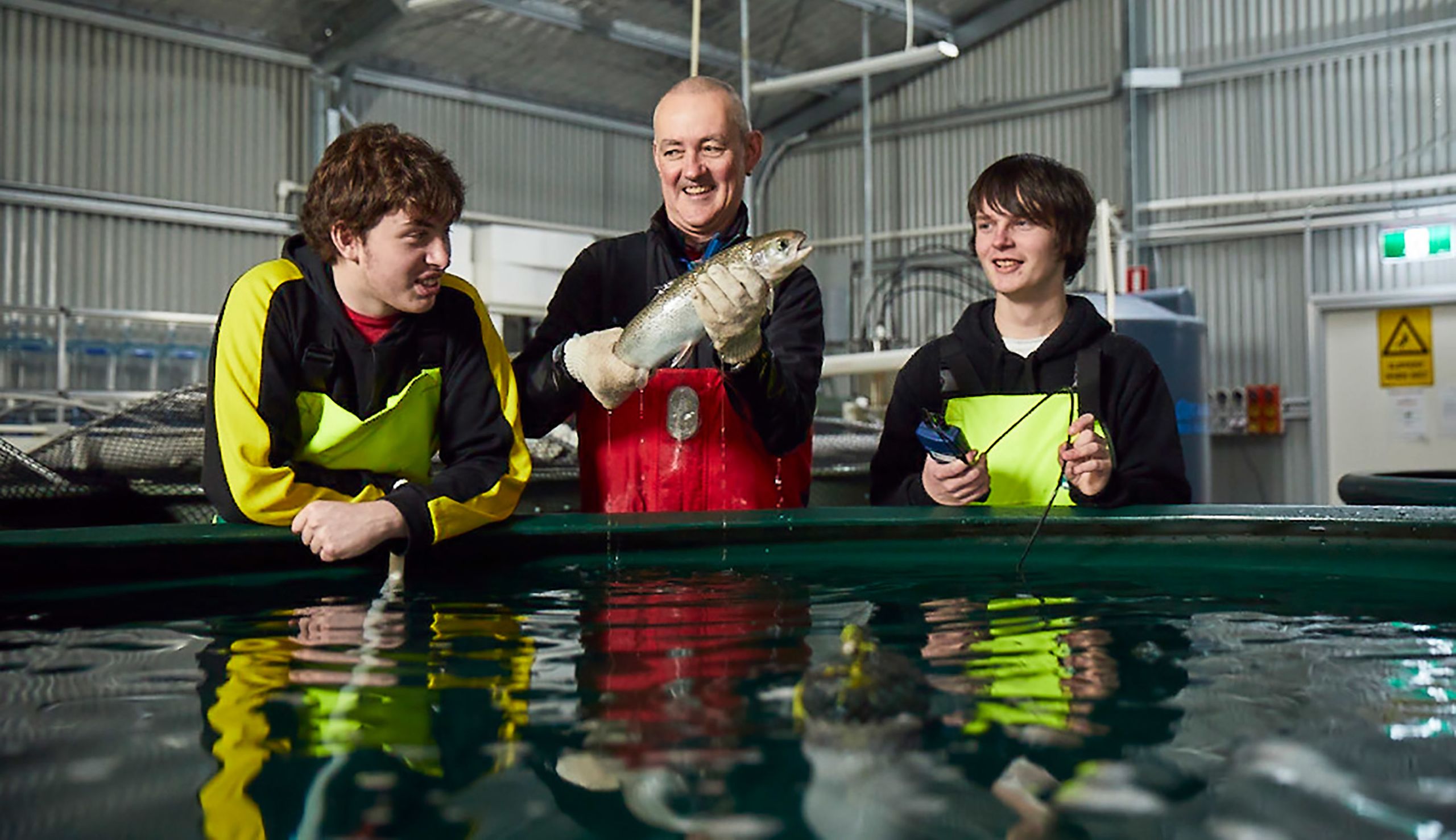 Steve Harrison holds fish from aquaculture tank as students watch