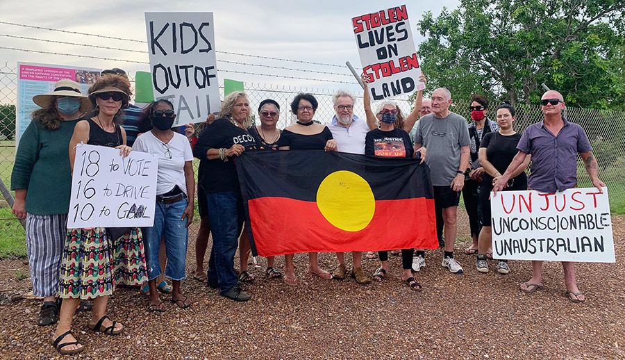 A group of protesters with an Aboriginal flag and several placards