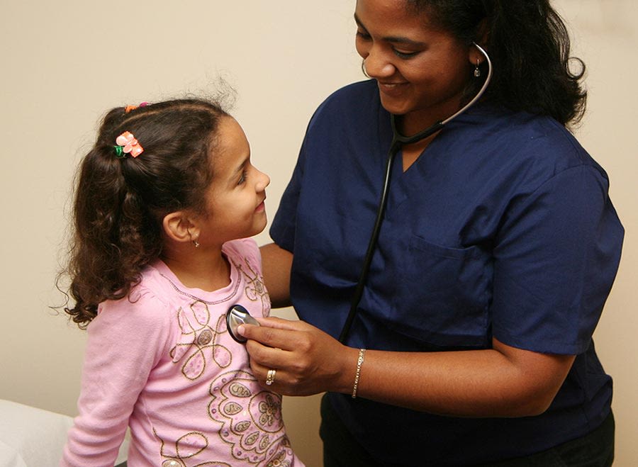 A health care professional using a stethoscope to listen to the heartbeat of a young girl
