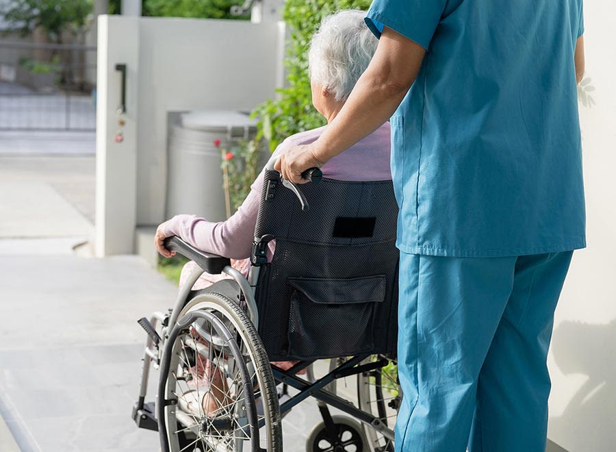 An image of an elderly woman in a wheelchair being pushed by a nurse.