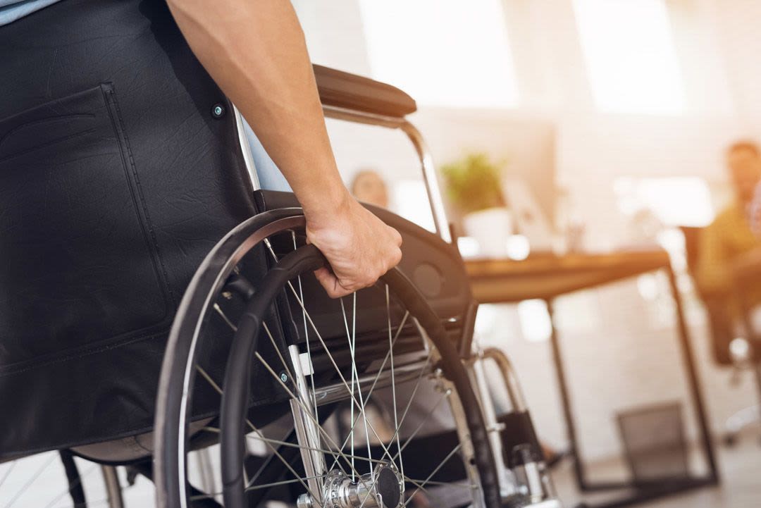 Cropped side-on photo of a hand gripping the wheel of a wheelchair