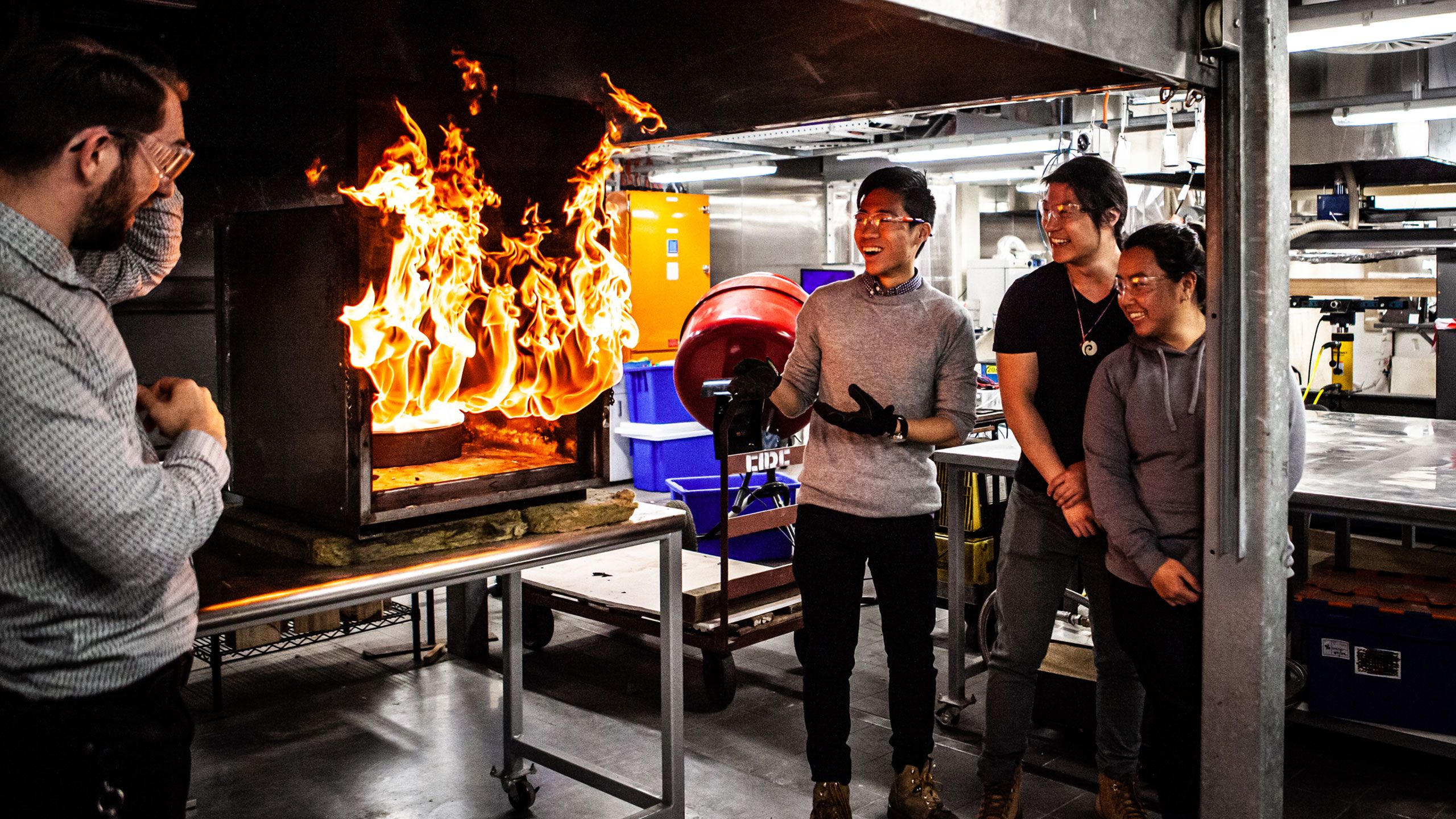 A researcher, a student and two graduates stand in front of massive flames during a compartment fire experiment