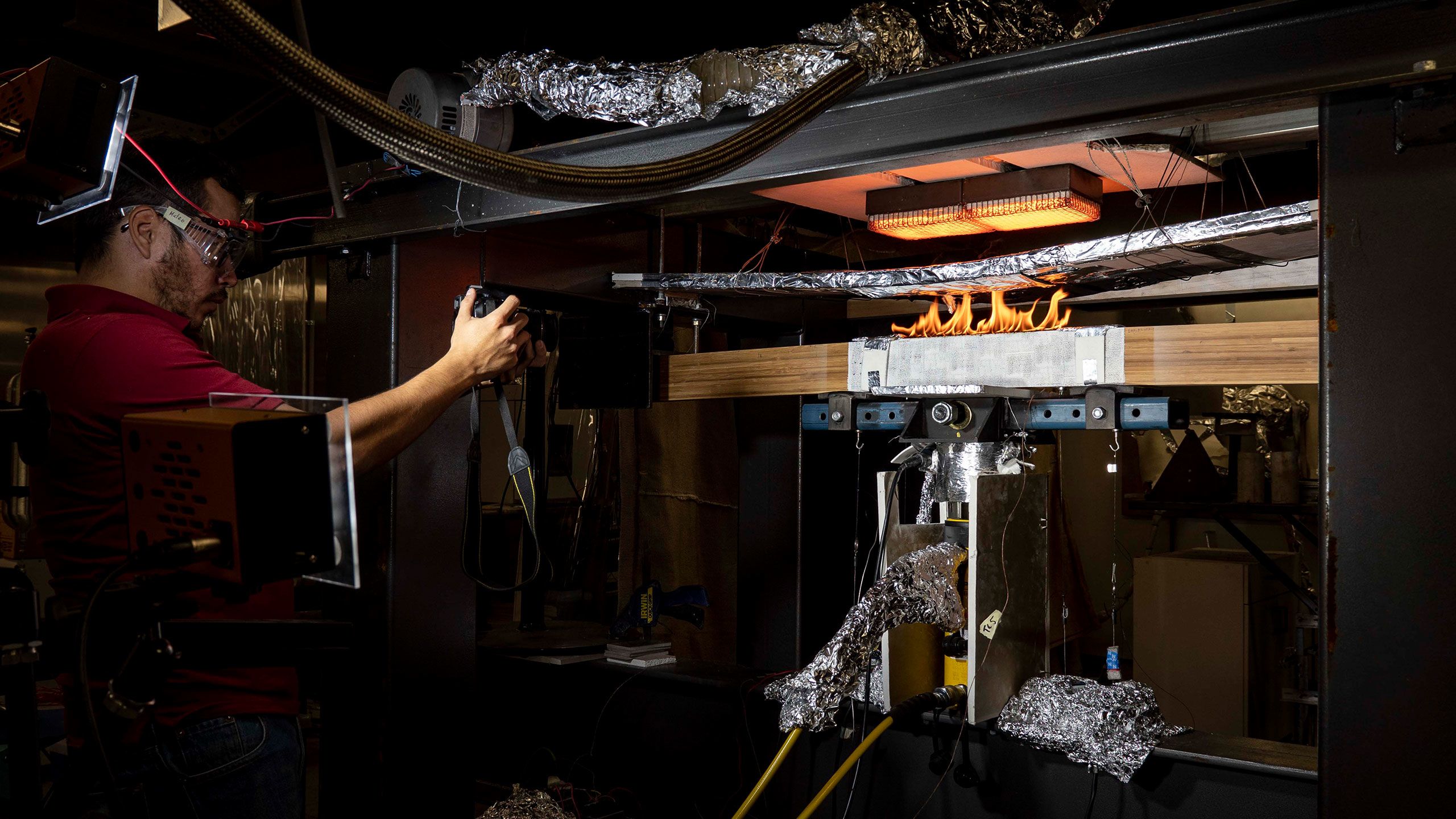 A male research scholar wearing safety glasses setting timber on fire at UQ's Fire Lab.