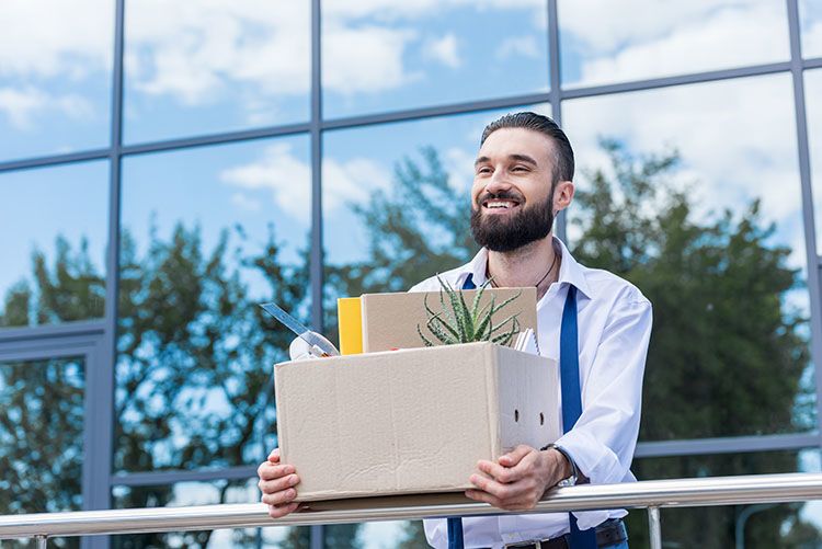Smiling man with a box of office supplies leaning on a rail