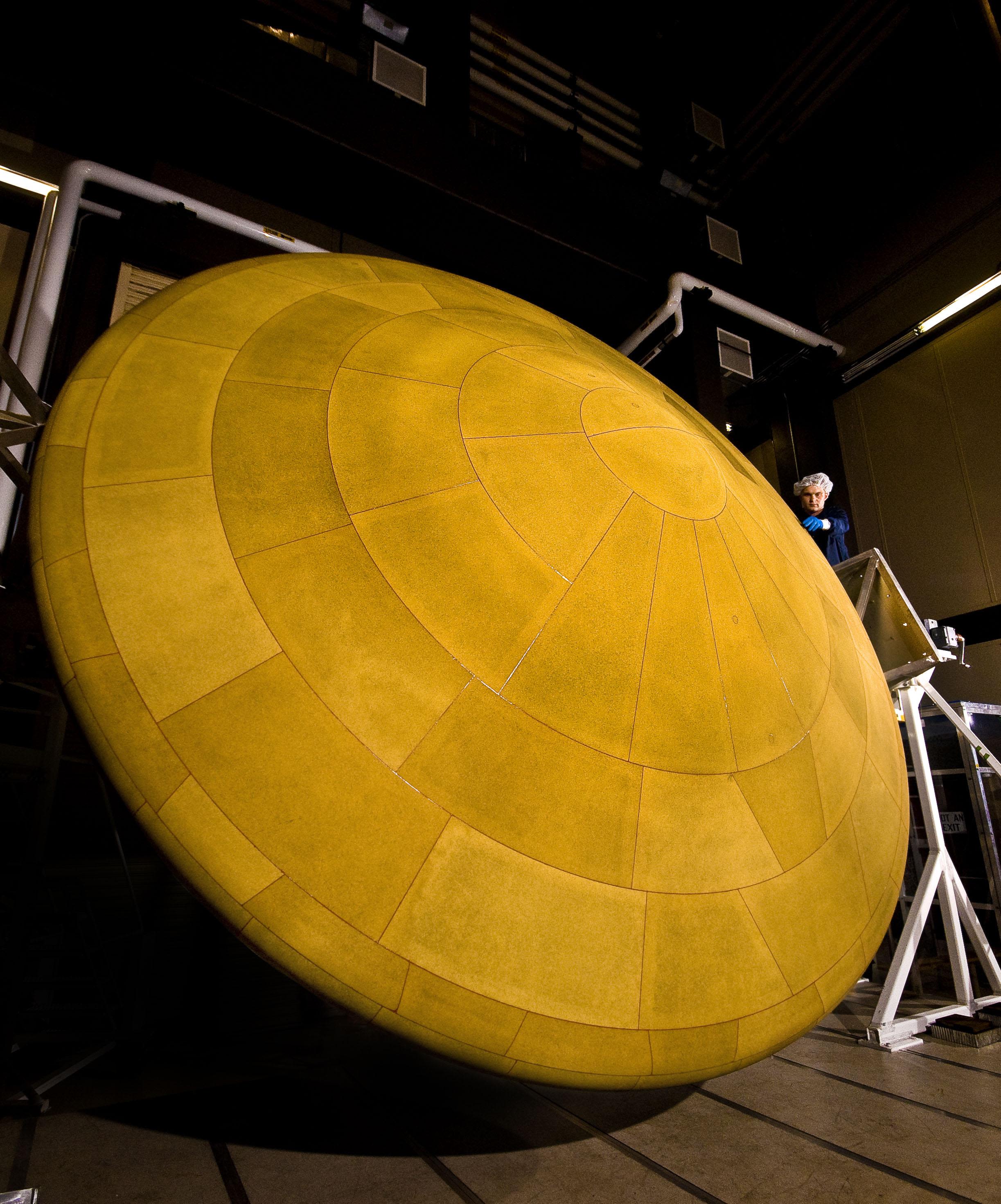 A spacecraft worker standing next to a huge heat shield.