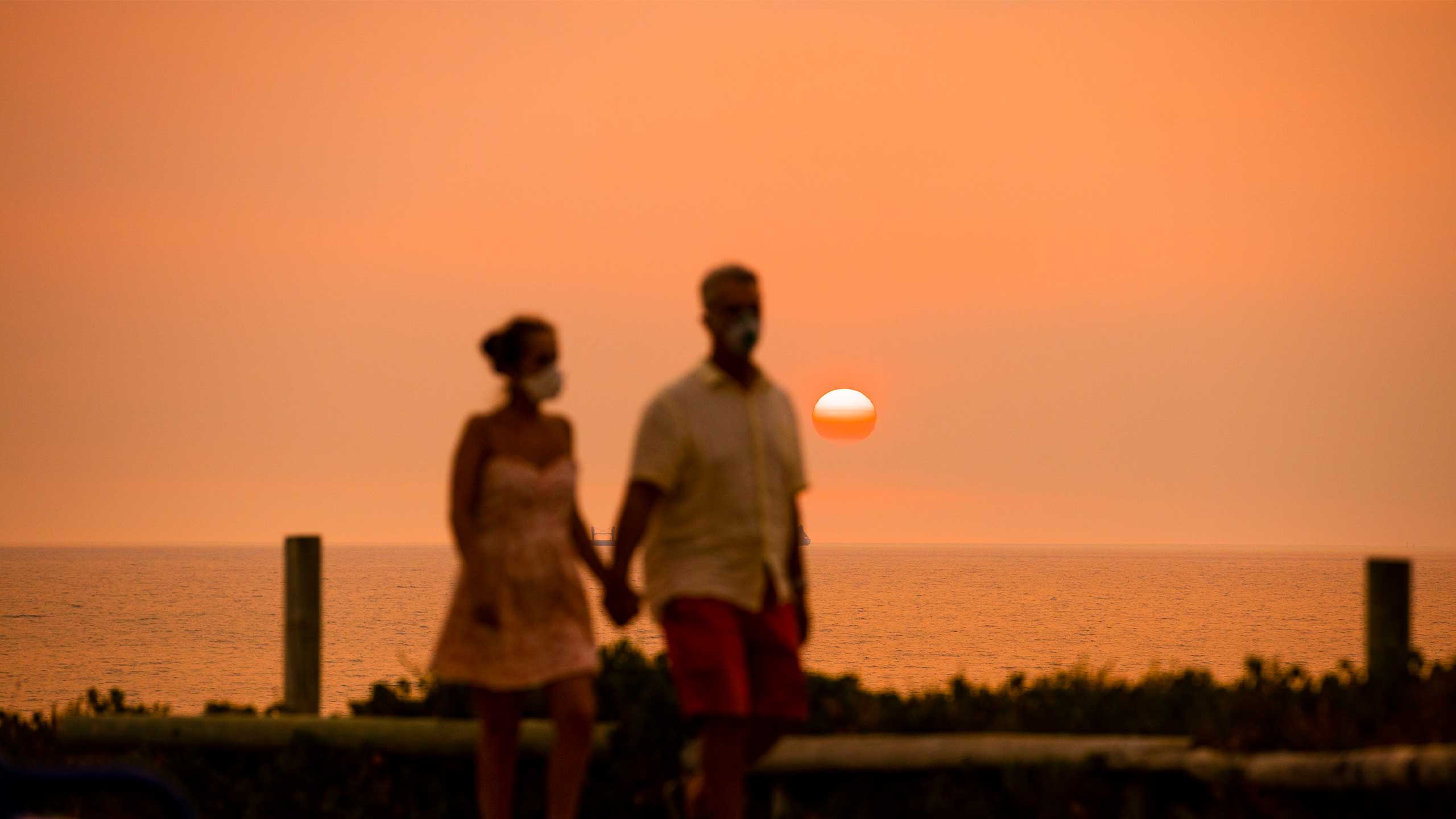 A man and woman are seen along a foreshore as the sun sets with smoke haze.