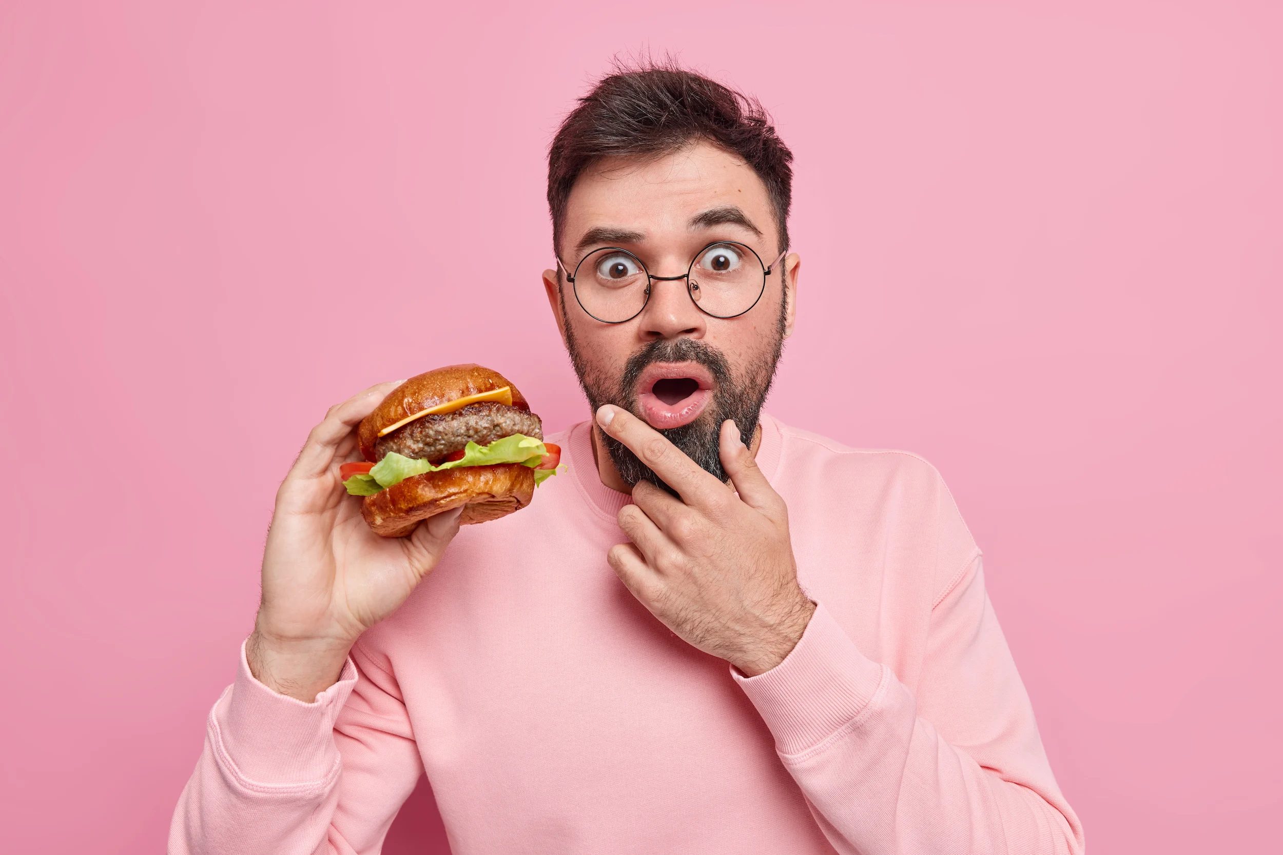 A man with a quizzical expression and his hand on his chin holding a cheeseburger