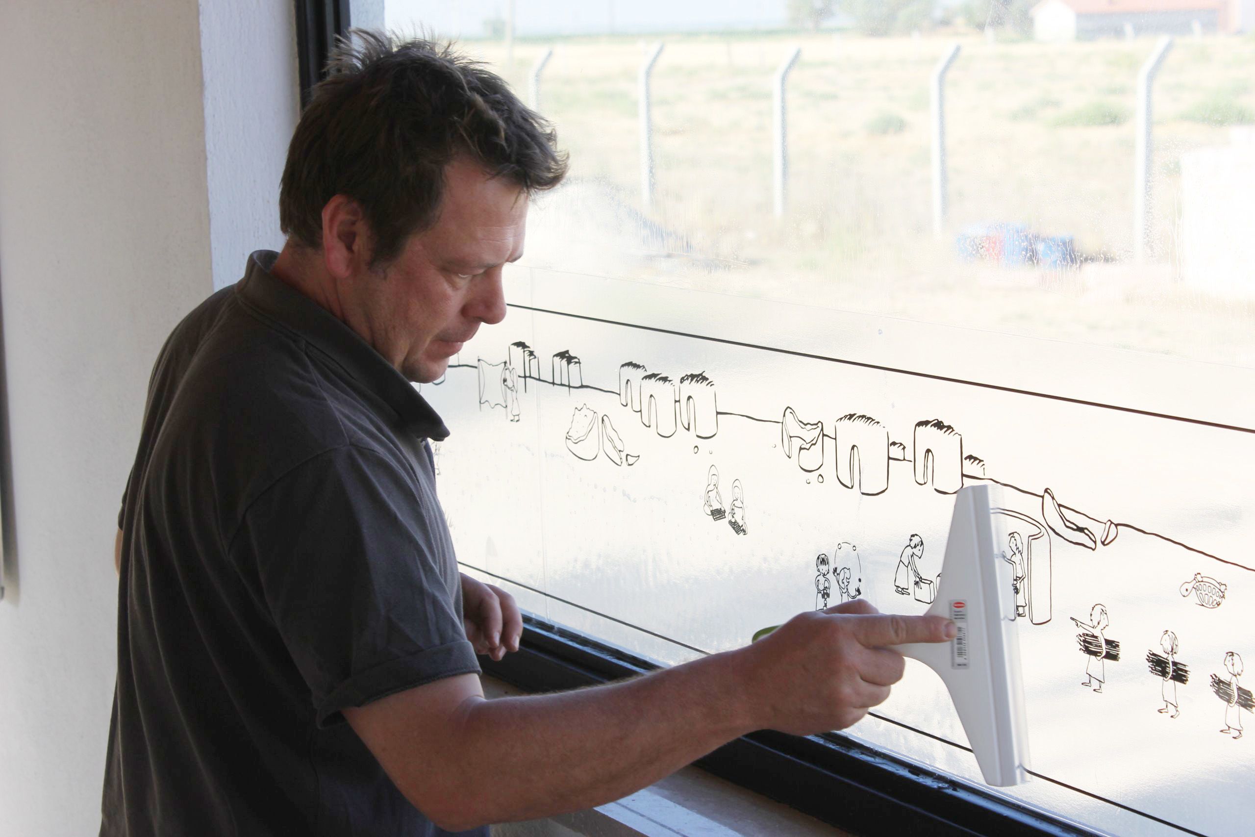 A man applies a transparent sticker showing a Neolithic village onto a window