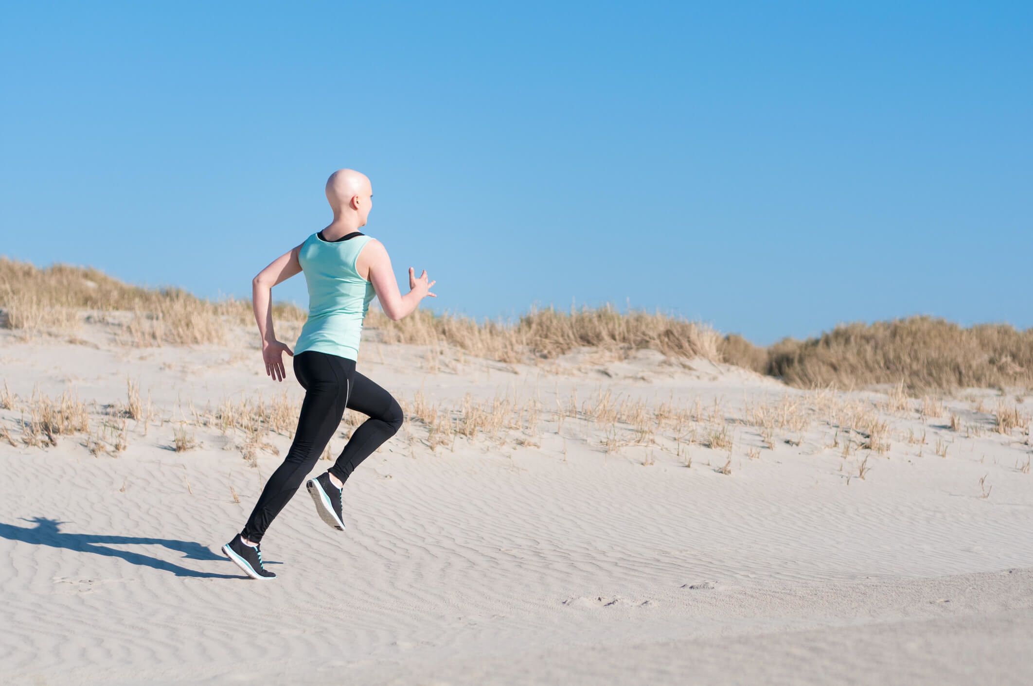 Woman with bald head running on beach