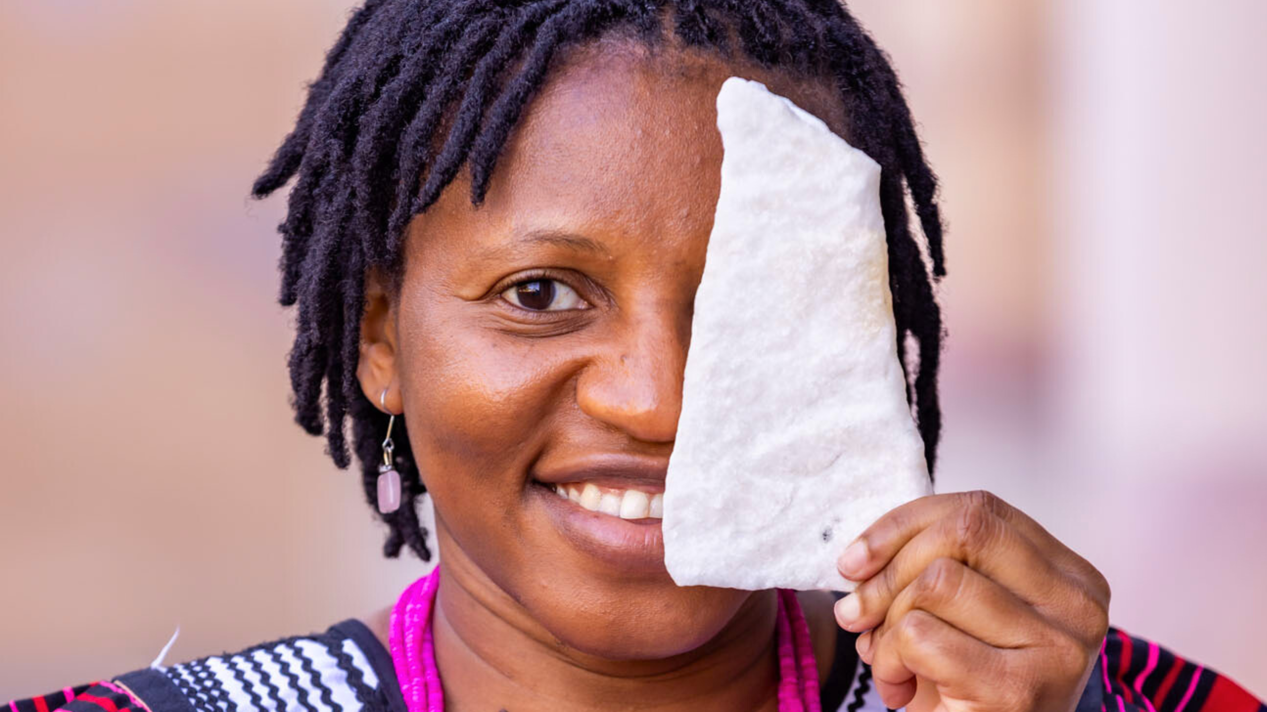 A close up of Linus's face, half obscured by a piece of stone she holds up against it.