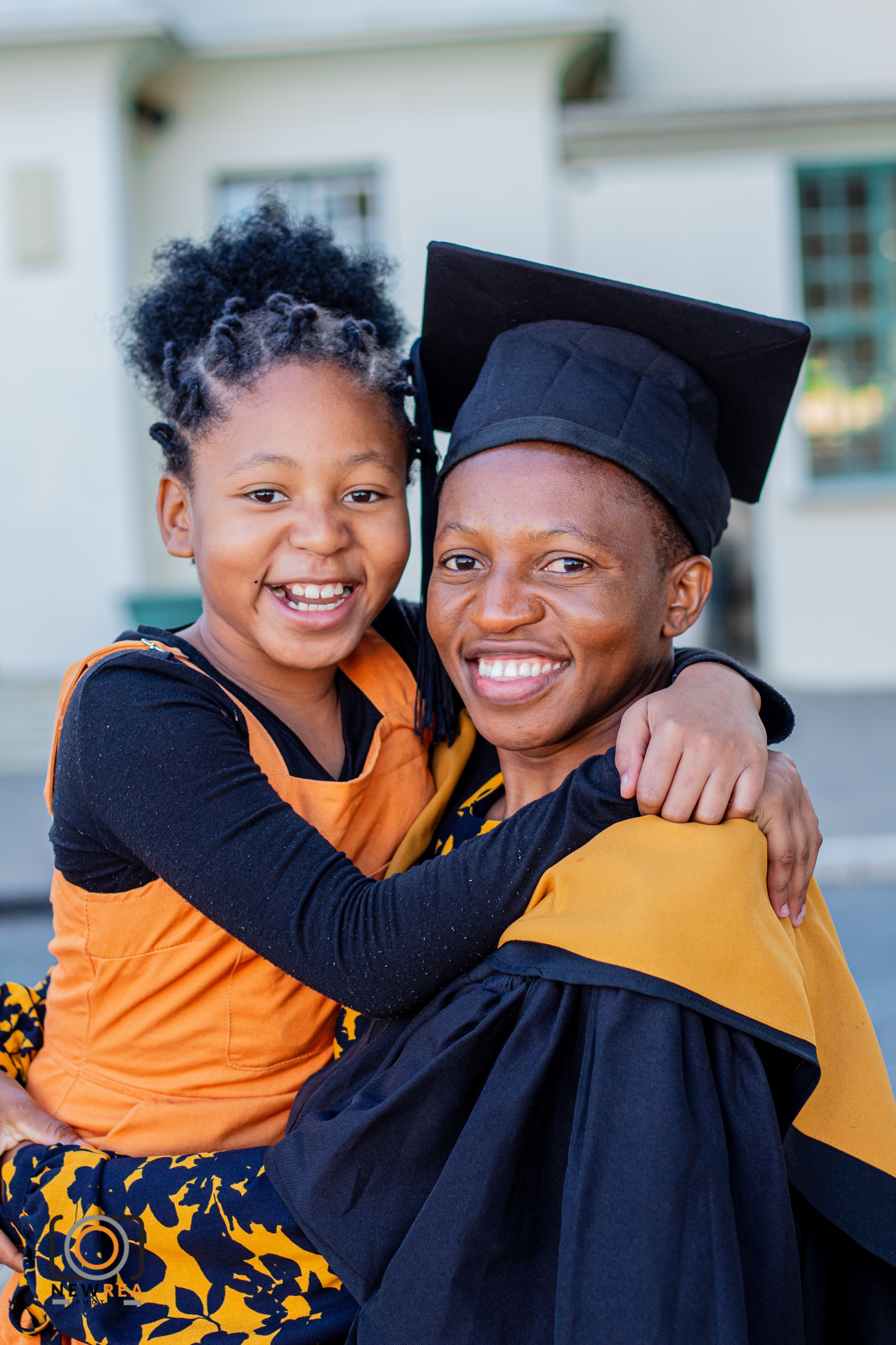 An portrait depicting Linus graduating from the University of Dundee dressed in her formal graduation robes. She holds her daughter close to her whose orange shirt matched the orange on her robe.
