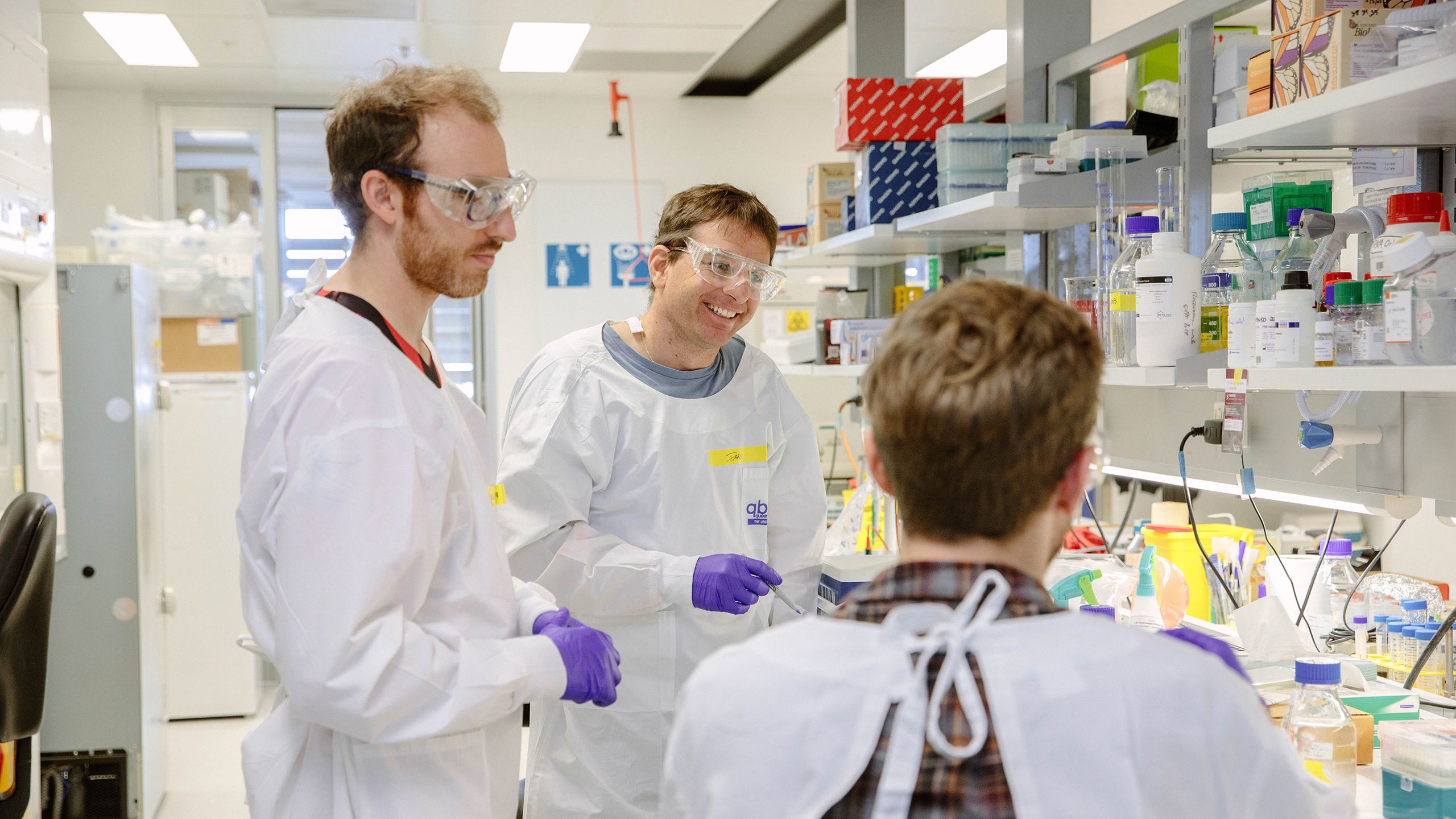 Three Queensland Brain Institute researchers in lab coats at a bench in a laboratory