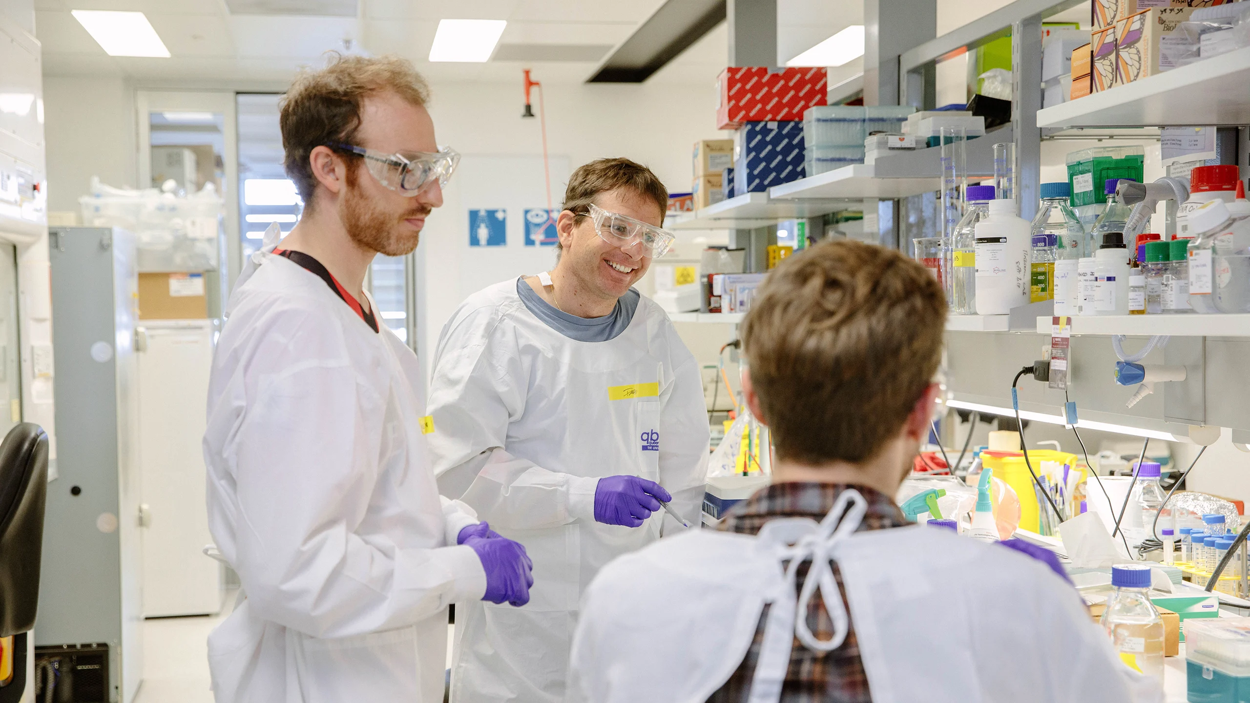 Three Queensland Brain Institute researchers in lab coats at a bench in a laboratory