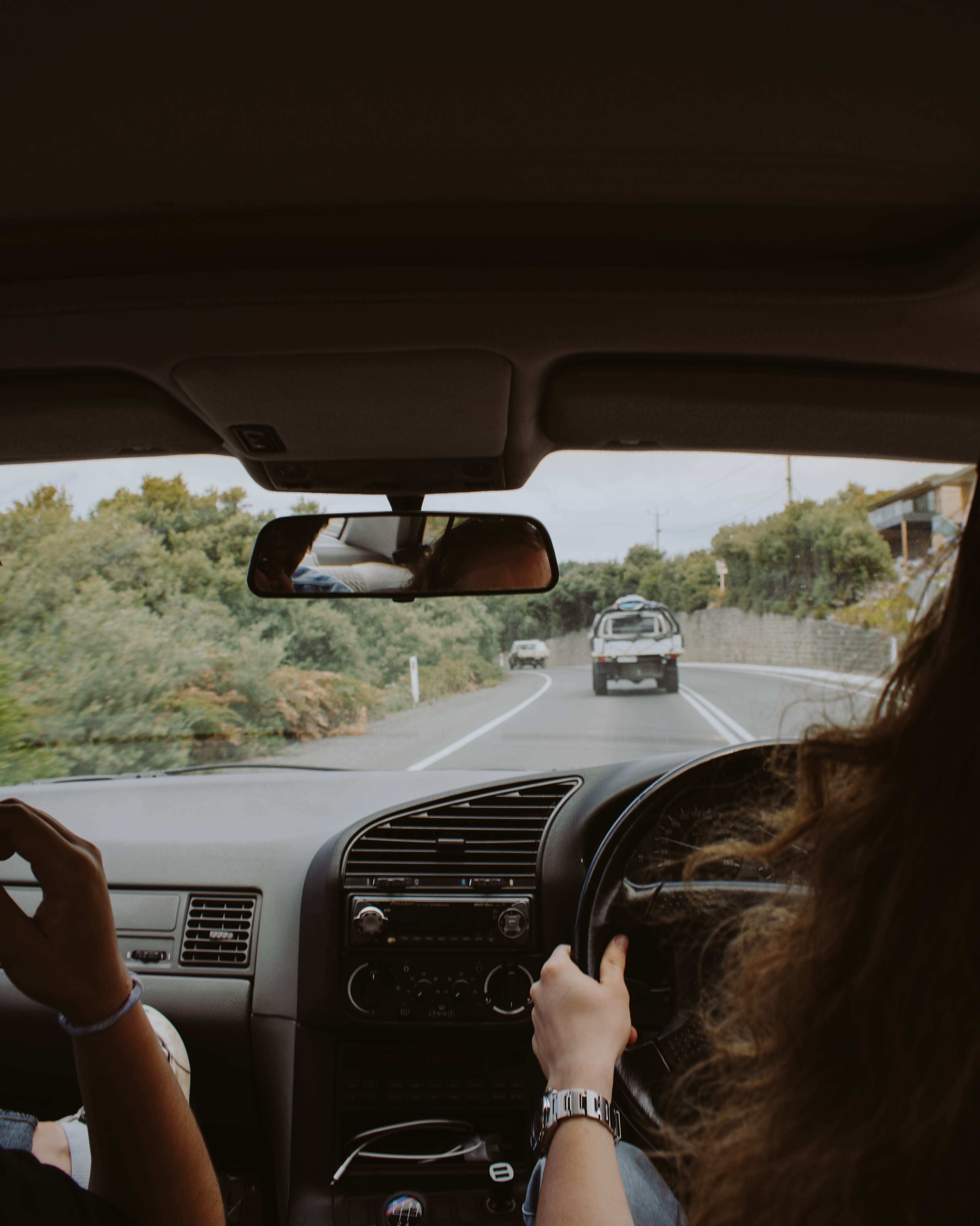 woman driving car on tree lined road during daytime