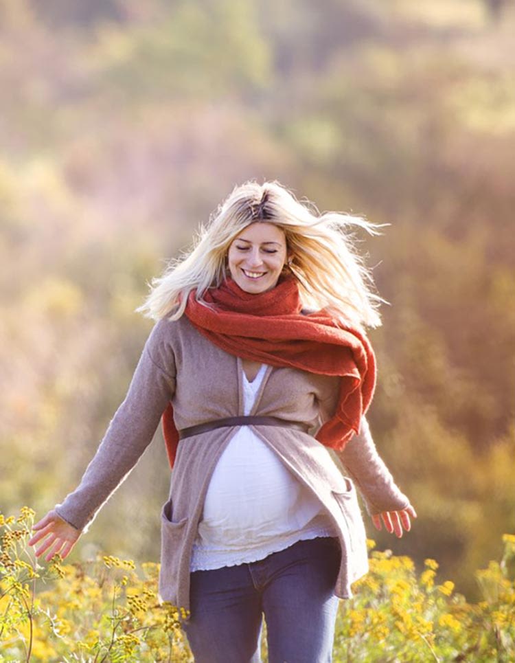 Pregnant woman walking through a field on a sunny day