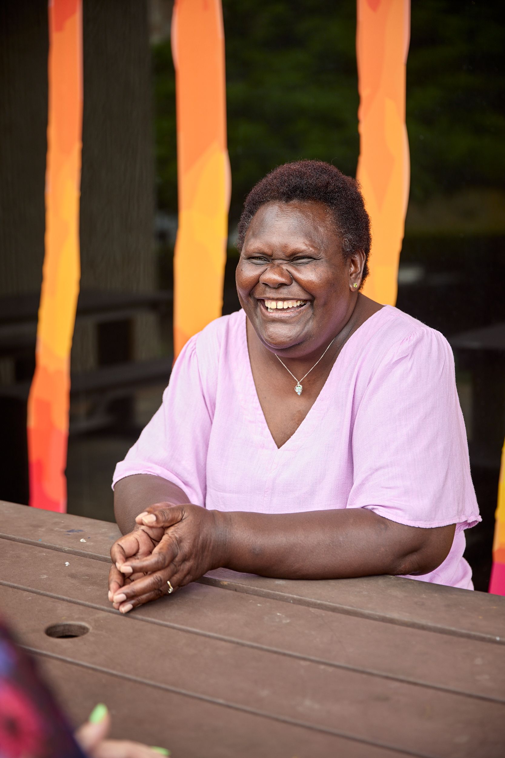A person is sitting and smiling wearing a pink linen top.
