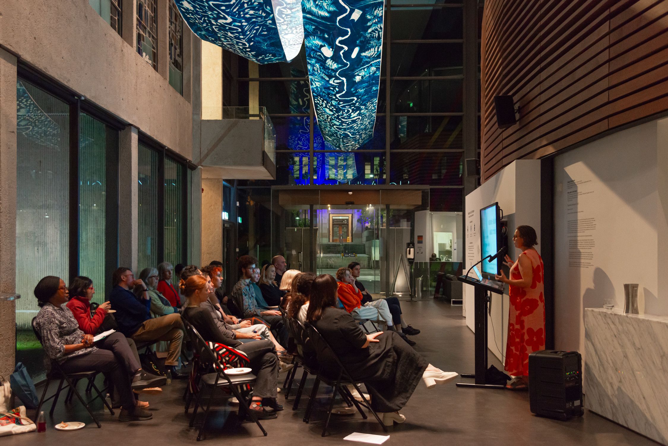 A group of people are seated facing a person deliver a lecture inside UQ Art Museum
