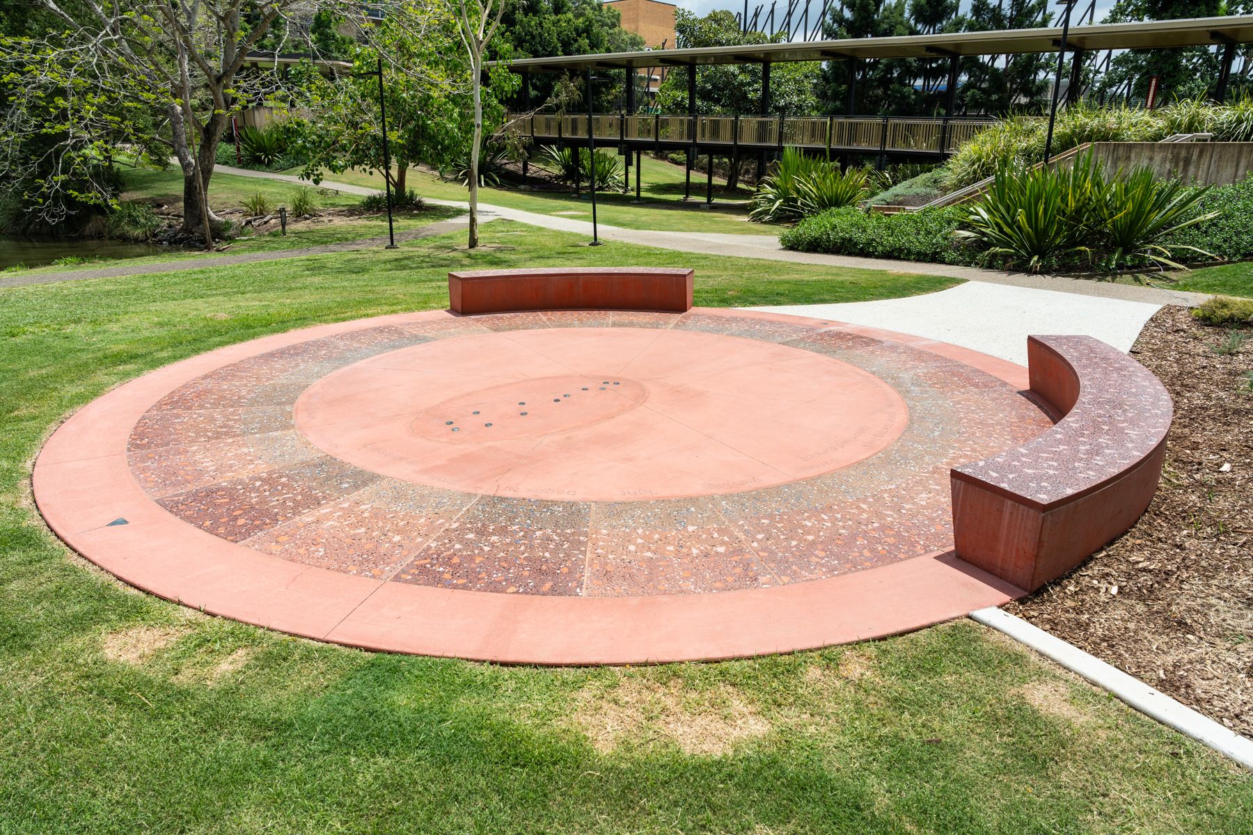 Public Artwork 'Sun Stadium' by Amrita Hepi. Red concrete sundial in the grass.