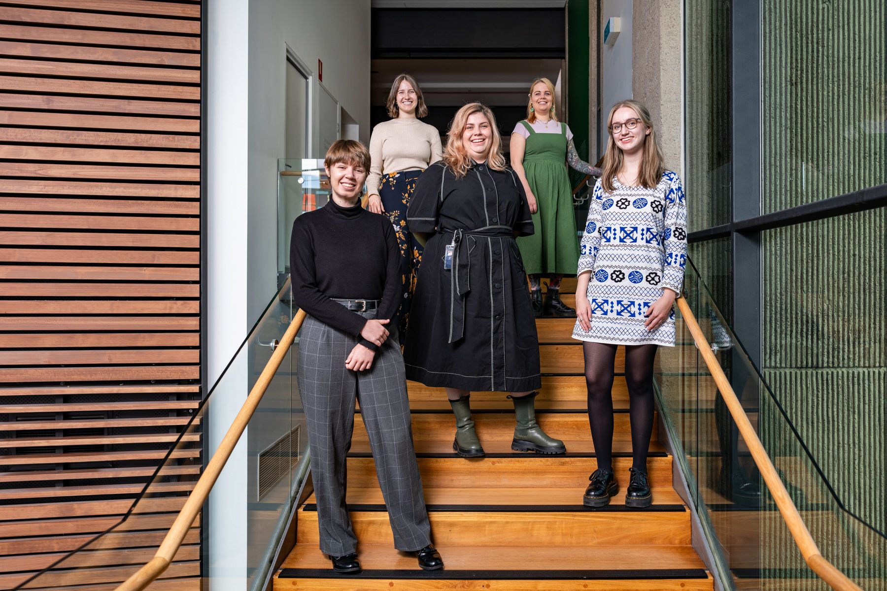 Five people standing on UQ Art Museum balcony stairs smiling and looking ahead.