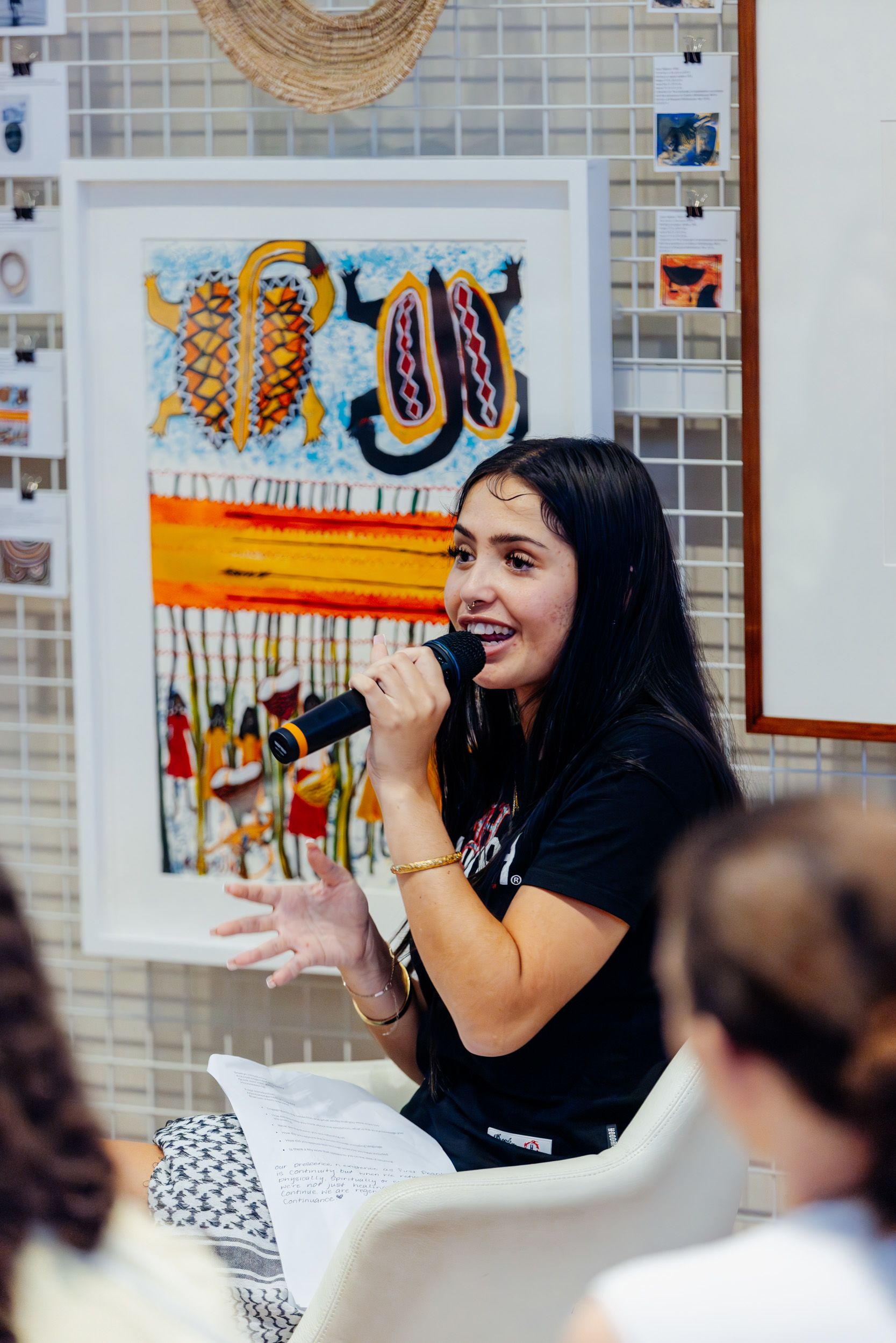 A person is sitting in front of a wall of artworks and talking into a microphone.