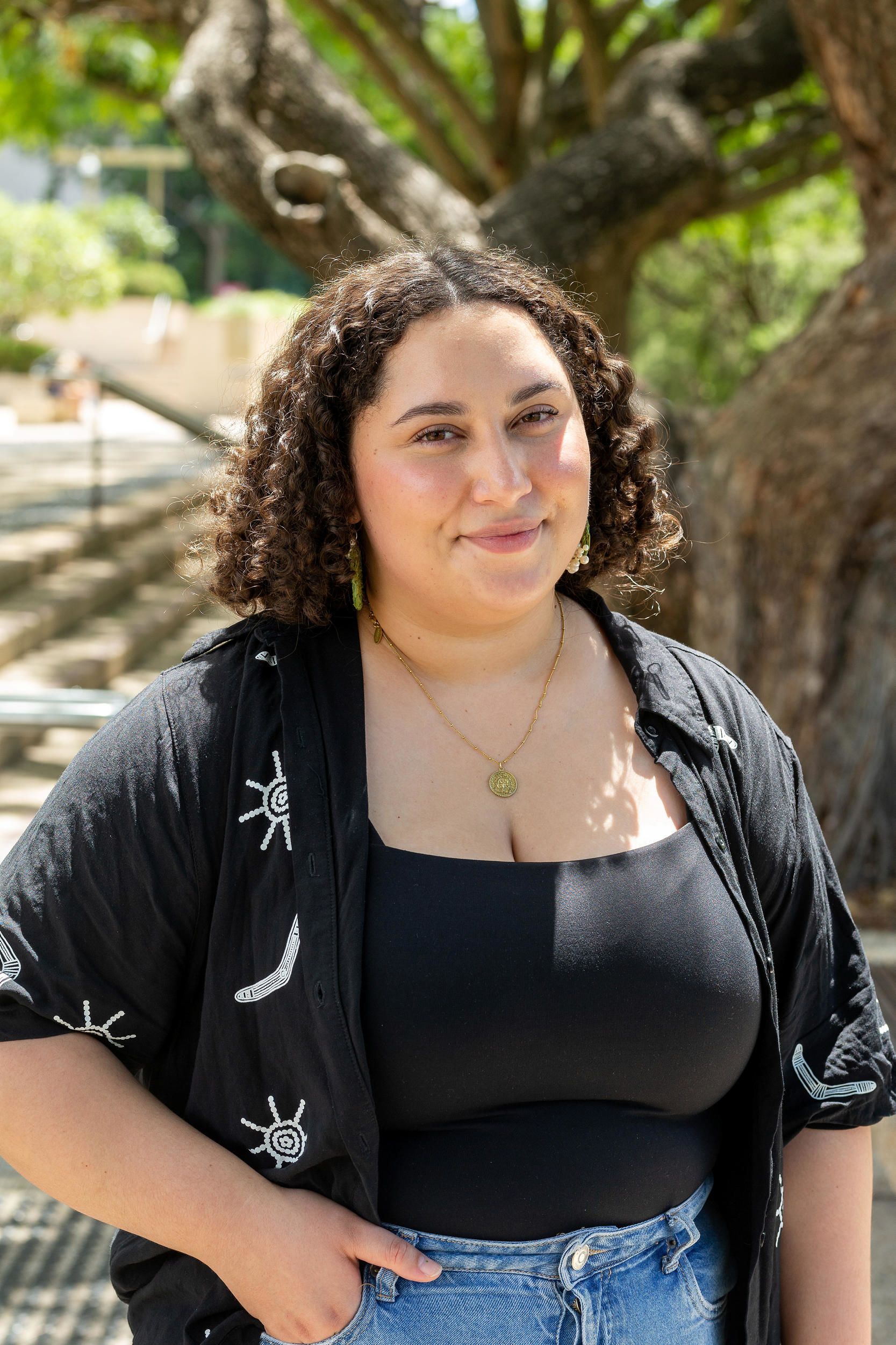 A person standing outside smiling. There are trees in the background.