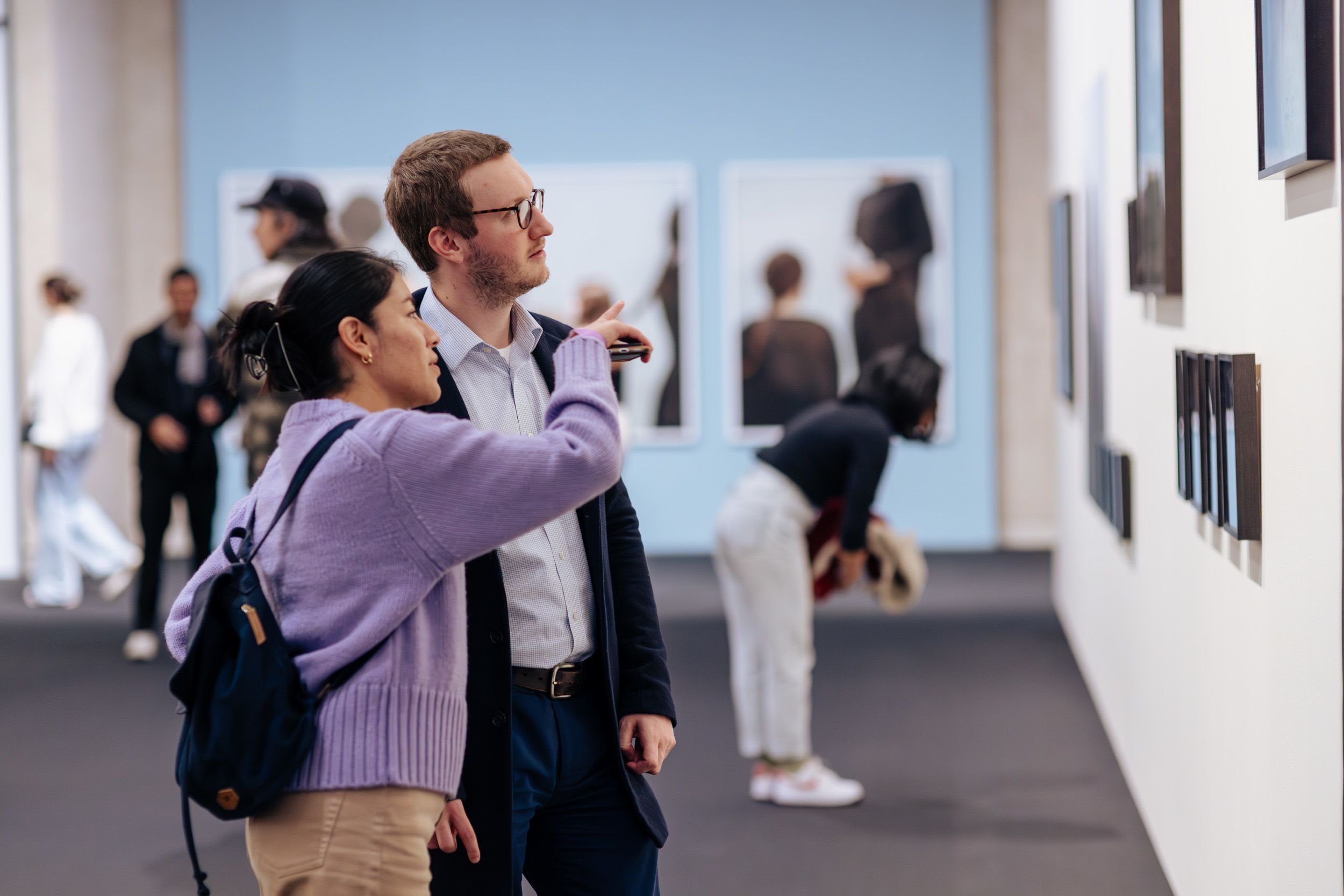 Two people visitors looking at Hoda Afshar's photographs hung inside UQ Art Museum. One visitor is pointing to a photograph. 