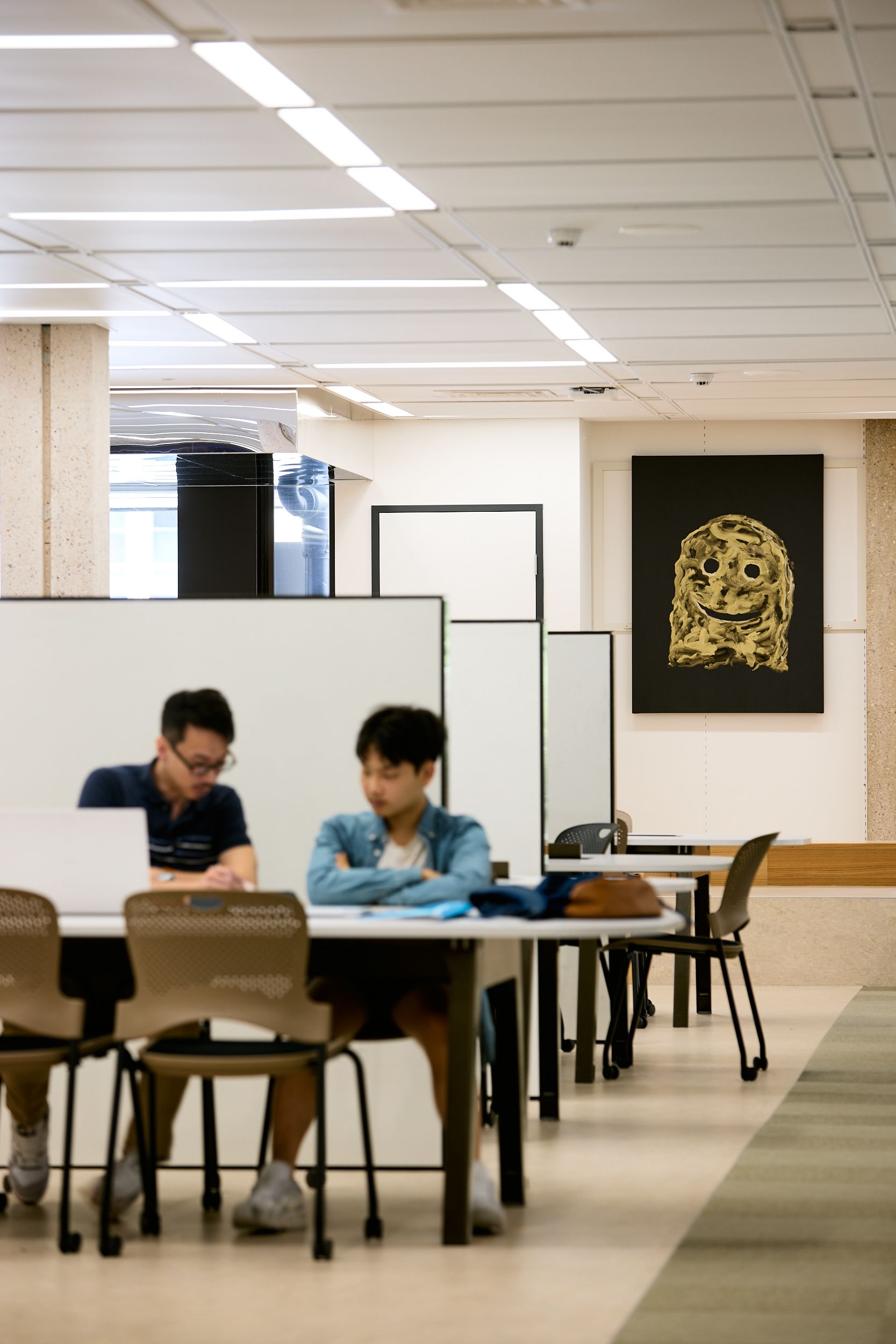 Two students studying in UQ Central Library. The painting 'Happy Ending' by Nell is hung on the wall behind them.
