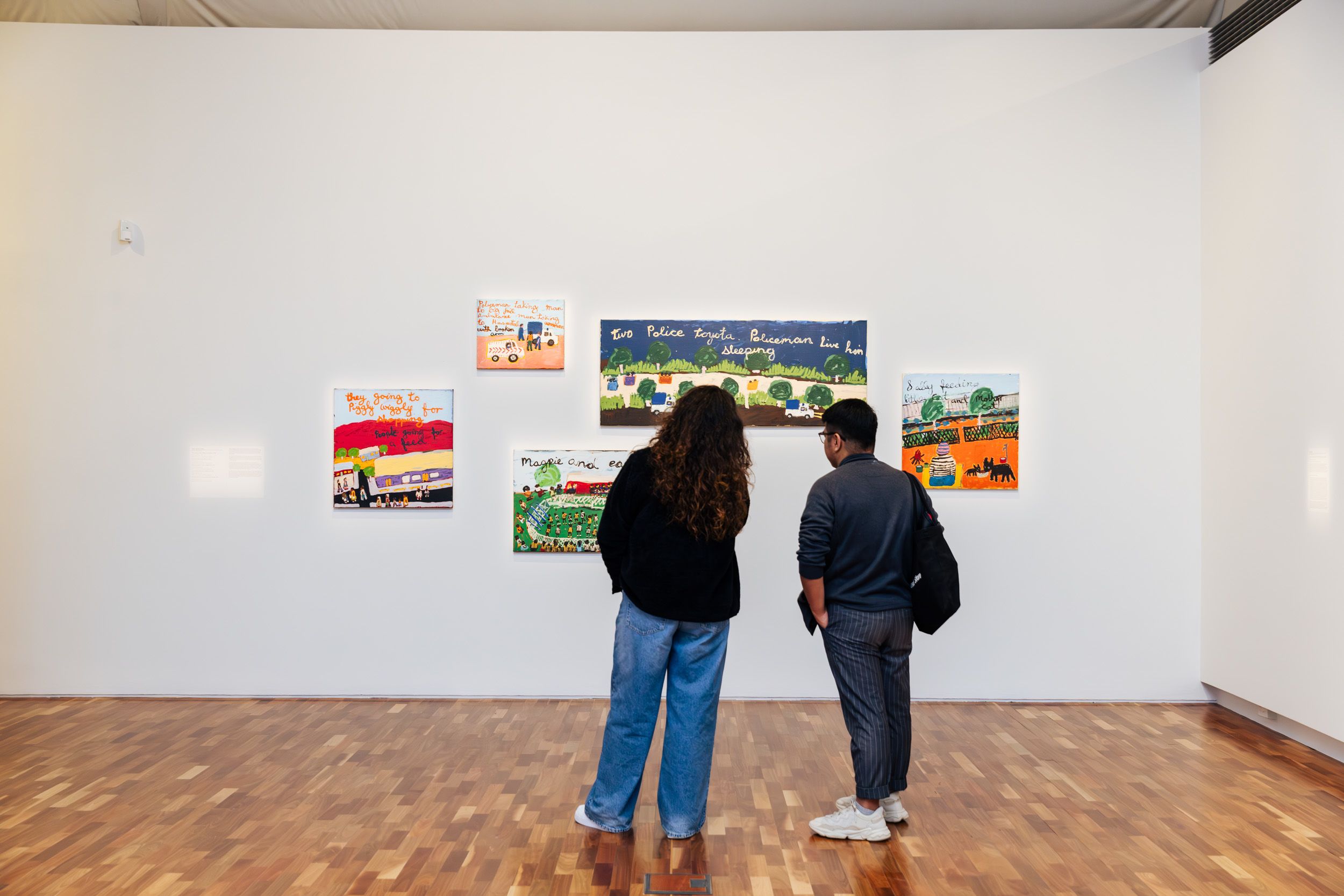 Two visitors stand in front of five paintings by Sally M. Nangala Mulda inside UQ Art Museum. 