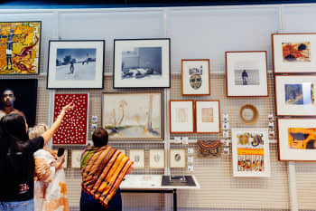 Three visitors are standing in front of wall of artworks hung in UQ Art Museum. One visitor is gesturing upwards towards the artworks.